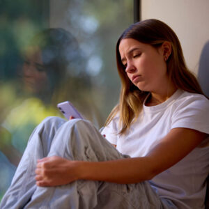 Depressed Teenage Girl Sitting By Window At Home