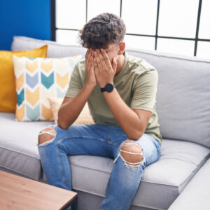 Young hispanic teenager stressed sitting on sofa at home