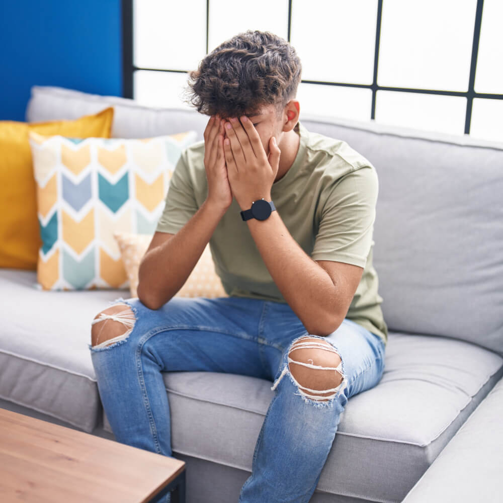 Young hispanic teenager stressed sitting on sofa at home