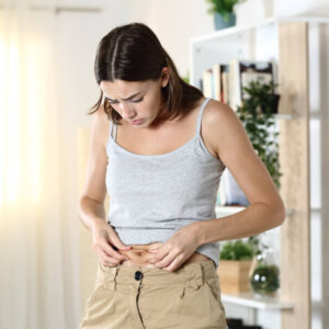 Woman worried about body fat touching her belly standing at home